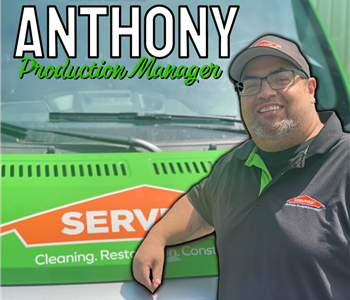 Man with dark hair and hat leaning on Green SERVPRO® truck to pose for photo